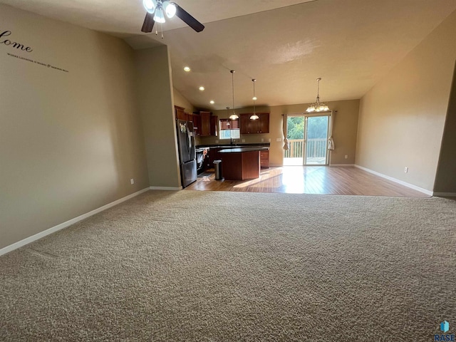 kitchen featuring freestanding refrigerator, vaulted ceiling, dark countertops, ceiling fan with notable chandelier, and open floor plan