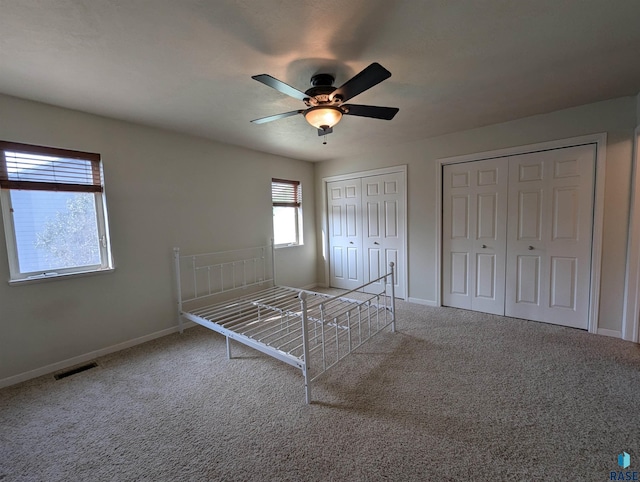 unfurnished bedroom with visible vents, two closets, ceiling fan, baseboards, and carpet floors