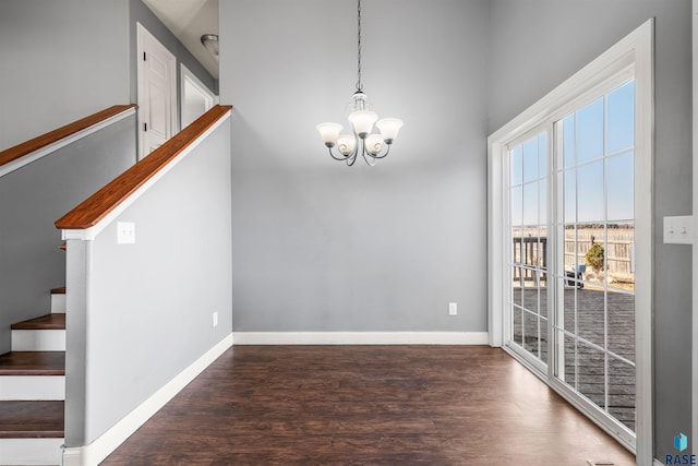 unfurnished dining area featuring a notable chandelier, stairs, baseboards, and wood finished floors