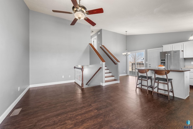 interior space with dark wood-style floors, baseboards, visible vents, lofted ceiling, and ceiling fan with notable chandelier