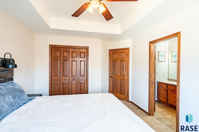 bedroom featuring a tray ceiling, light colored carpet, a closet, and baseboards