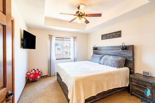 bedroom with baseboards, light colored carpet, a tray ceiling, a textured ceiling, and a ceiling fan