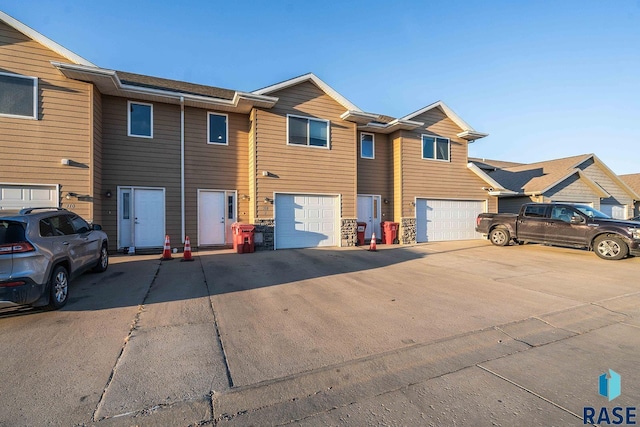 townhome / multi-family property with stone siding, driveway, and a garage