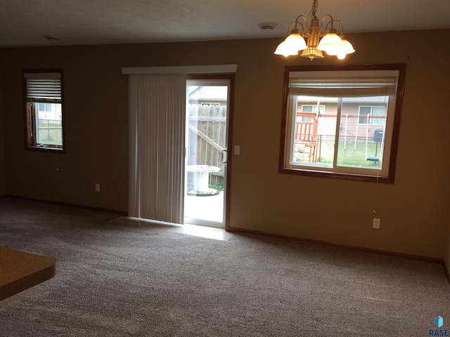 unfurnished room with baseboards, plenty of natural light, carpet, and an inviting chandelier