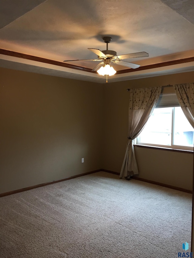 carpeted empty room with a raised ceiling, baseboards, and ceiling fan