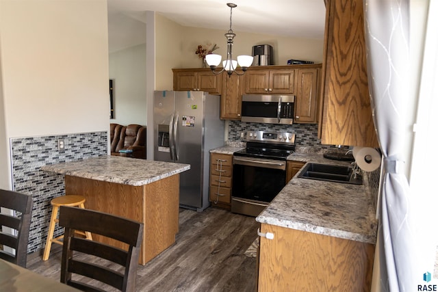 kitchen with dark wood finished floors, appliances with stainless steel finishes, a peninsula, brown cabinetry, and lofted ceiling