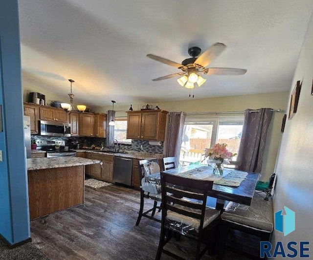 kitchen with a sink, stainless steel appliances, dark wood-type flooring, ceiling fan with notable chandelier, and backsplash