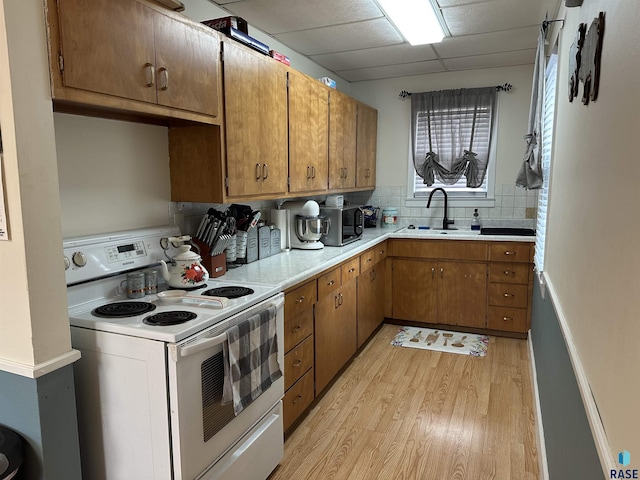 kitchen featuring light wood-type flooring, light countertops, decorative backsplash, white electric stove, and a sink