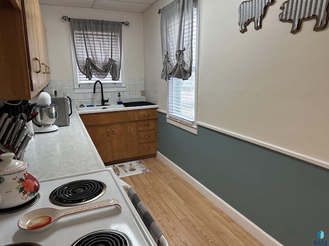 kitchen featuring light wood-type flooring, light countertops, decorative backsplash, brown cabinets, and a sink