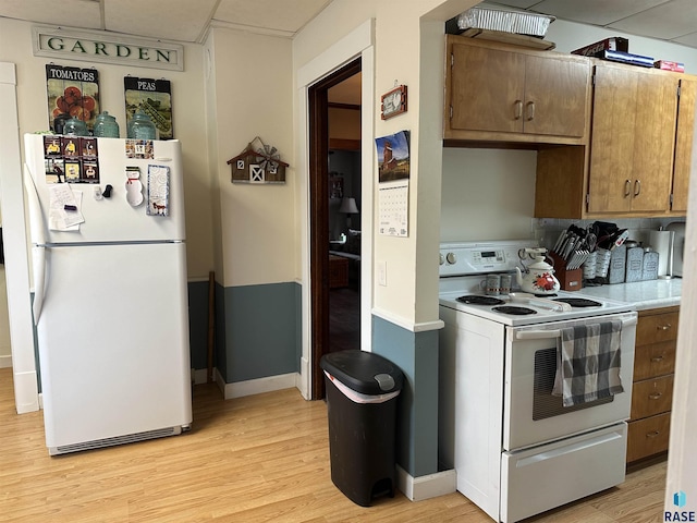 kitchen with light wood finished floors, baseboards, white appliances, light countertops, and a paneled ceiling