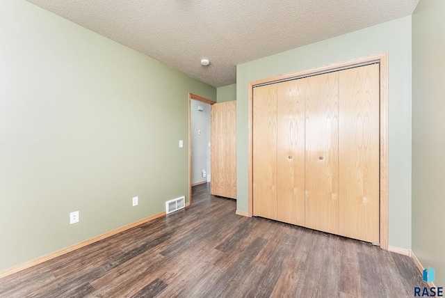 unfurnished bedroom featuring visible vents, a textured ceiling, wood finished floors, a closet, and baseboards