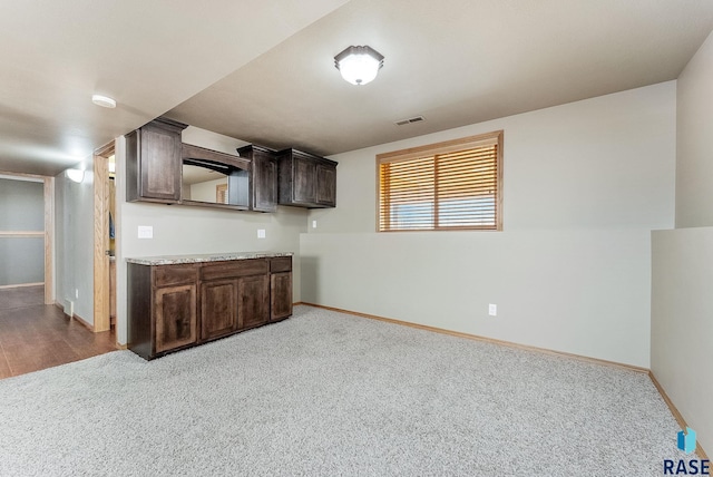 kitchen featuring visible vents, dark brown cabinets, baseboards, light countertops, and carpet floors