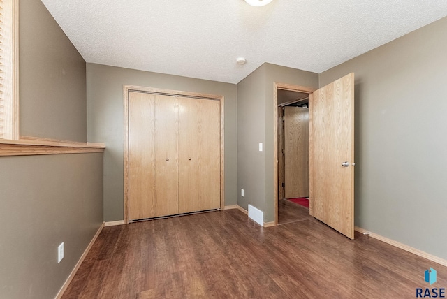 unfurnished bedroom with a textured ceiling, wood finished floors, a closet, and baseboards