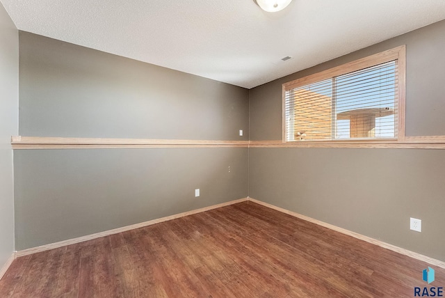 empty room featuring a textured ceiling, baseboards, and wood finished floors