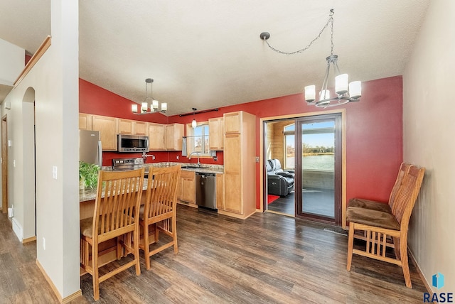 kitchen featuring dark wood finished floors, stainless steel appliances, light brown cabinetry, vaulted ceiling, and a chandelier