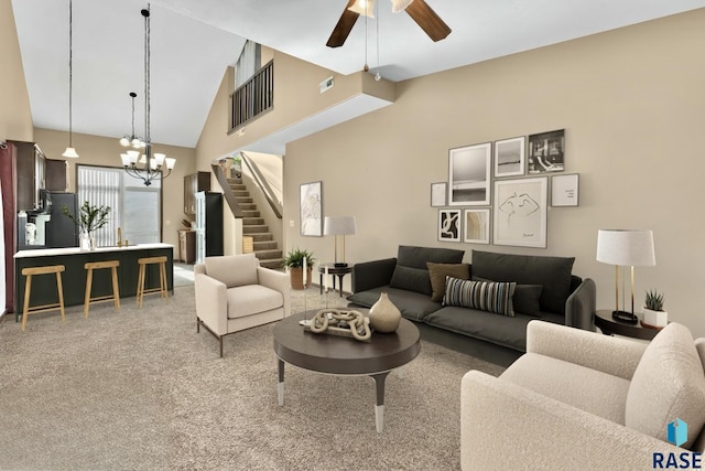 living area with stairway, high vaulted ceiling, carpet flooring, and ceiling fan with notable chandelier