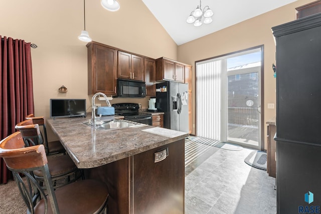 kitchen with black appliances, a sink, a kitchen breakfast bar, dark brown cabinetry, and hanging light fixtures