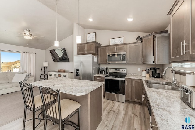 kitchen with a ceiling fan, a sink, open floor plan, stainless steel appliances, and a breakfast bar area