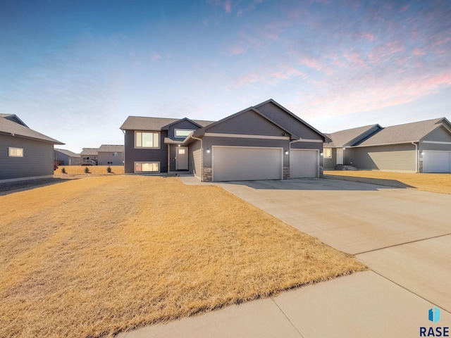 view of front of house with a garage, stone siding, a yard, and concrete driveway