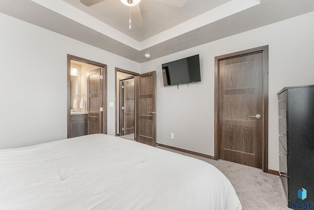 bedroom with a ceiling fan, a tray ceiling, ensuite bath, carpet, and baseboards