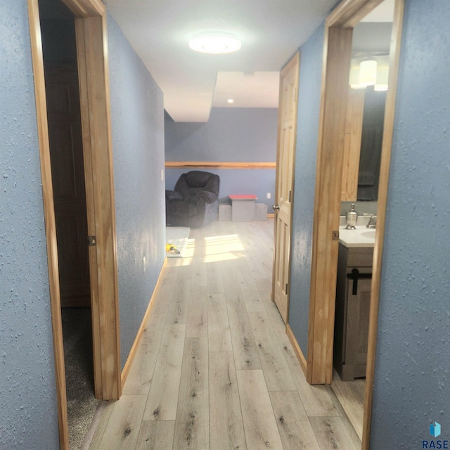 hall featuring light wood finished floors, baseboards, and a textured wall