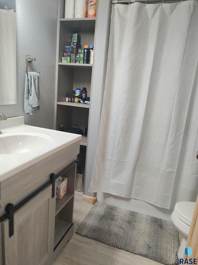 full bath with curtained shower, toilet, wood finished floors, a textured wall, and vanity