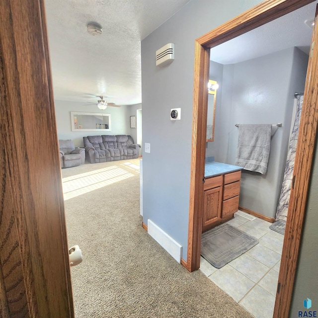 corridor featuring a textured ceiling, baseboards, visible vents, and light carpet