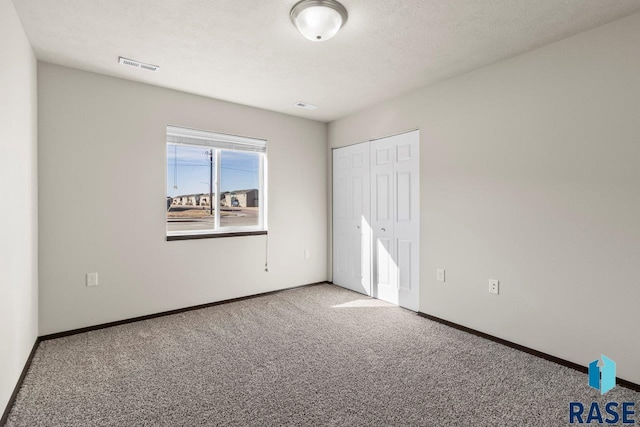 unfurnished bedroom with visible vents, baseboards, carpet flooring, a closet, and a textured ceiling