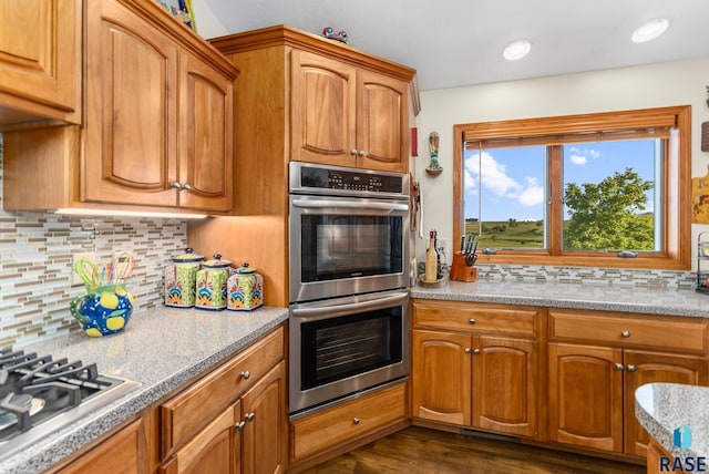 kitchen featuring brown cabinetry, decorative backsplash, stainless steel appliances, and dark wood-type flooring