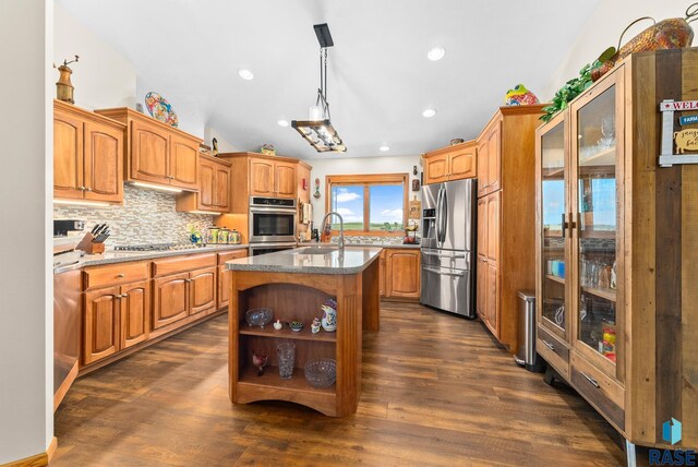 kitchen featuring a center island with sink, a sink, backsplash, dark wood-style floors, and stainless steel appliances