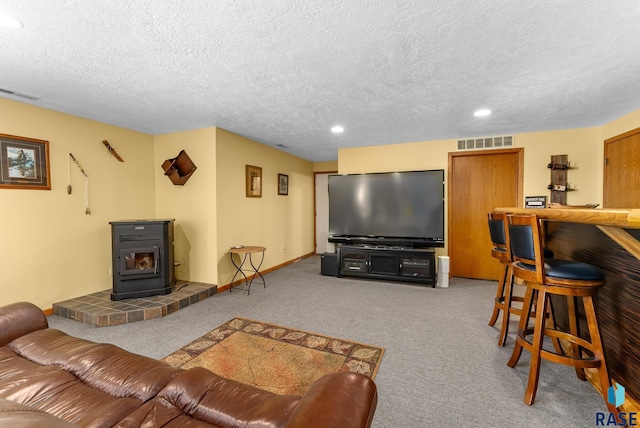 carpeted living area featuring a wood stove, baseboards, visible vents, and a textured ceiling