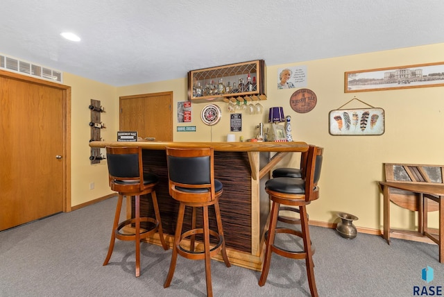 bar with visible vents, a textured ceiling, carpet floors, a bar, and baseboards