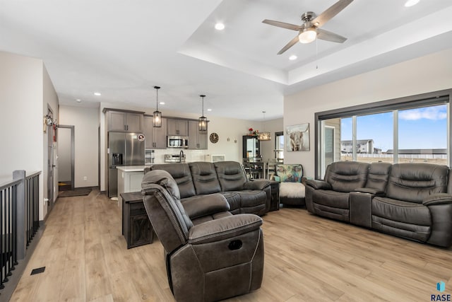 living area featuring light wood finished floors, recessed lighting, a raised ceiling, and ceiling fan
