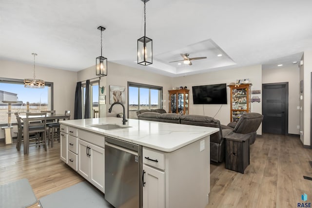 kitchen with ceiling fan, light wood-type flooring, a tray ceiling, stainless steel dishwasher, and a sink