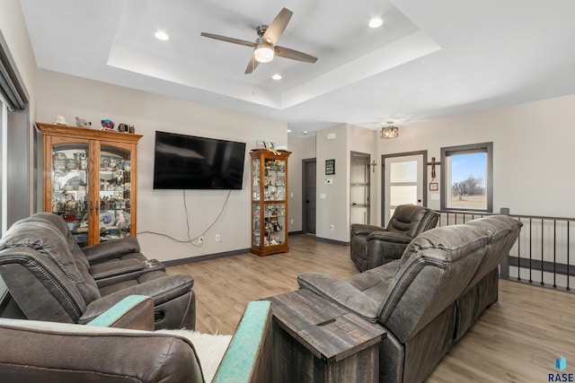 living room with baseboards, a ceiling fan, light wood-style floors, and a tray ceiling