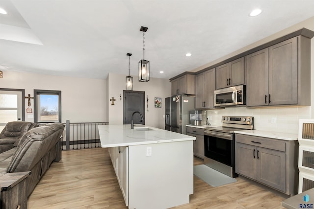 kitchen with light wood finished floors, open floor plan, decorative backsplash, appliances with stainless steel finishes, and a sink