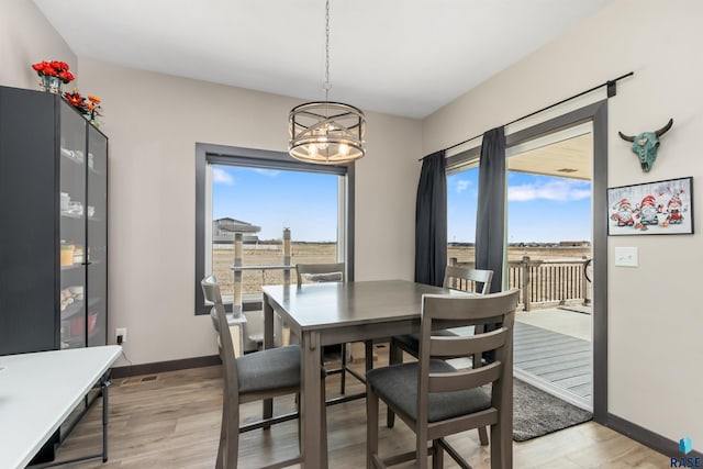 dining room with a wealth of natural light, light wood-style floors, baseboards, and a notable chandelier