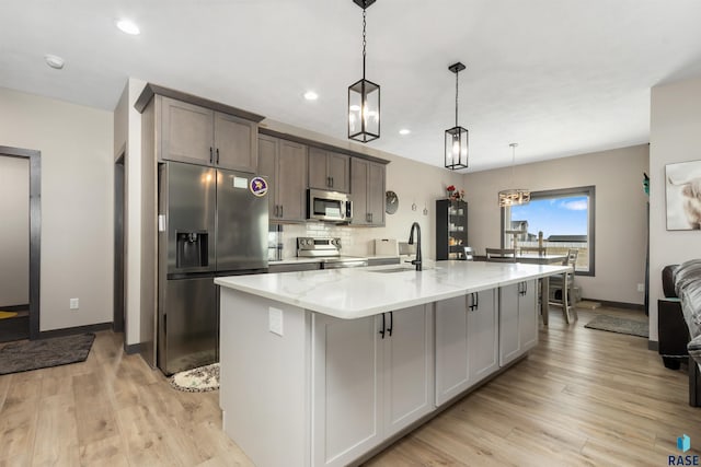 kitchen featuring a sink, appliances with stainless steel finishes, a center island with sink, and light wood finished floors