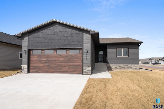 view of front of property featuring driveway, stone siding, roof with shingles, a front yard, and a garage