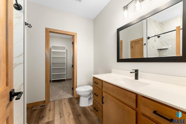 bathroom with vanity, wood finished floors, visible vents, a walk in closet, and toilet