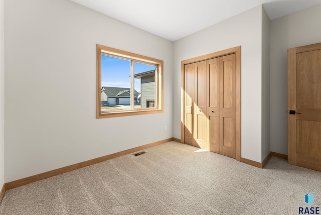 unfurnished bedroom featuring visible vents, light colored carpet, baseboards, and a closet