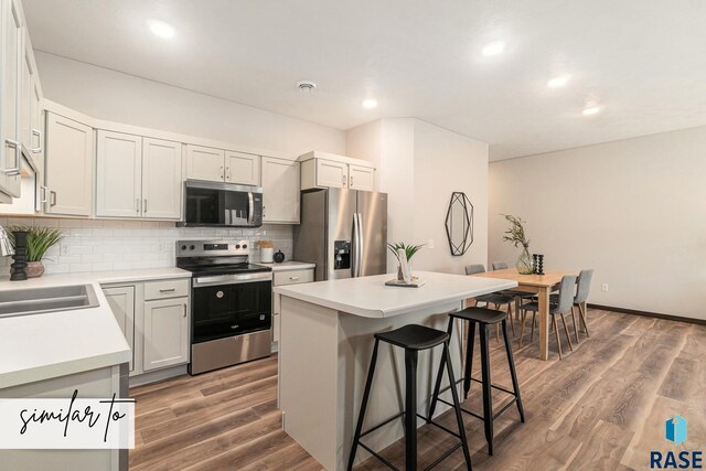 5714 E Avett Pl, Sioux Falls, SD 57108 - kitchen featuring a kitchen island, a kitchen bar, decorative backsplash, wood finished floors, and stainless steel appliances