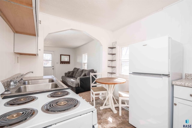 kitchen with white appliances, arched walkways, a sink, light countertops, and a textured ceiling