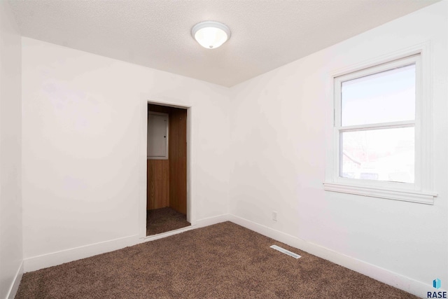 spare room with baseboards, a textured ceiling, and dark carpet