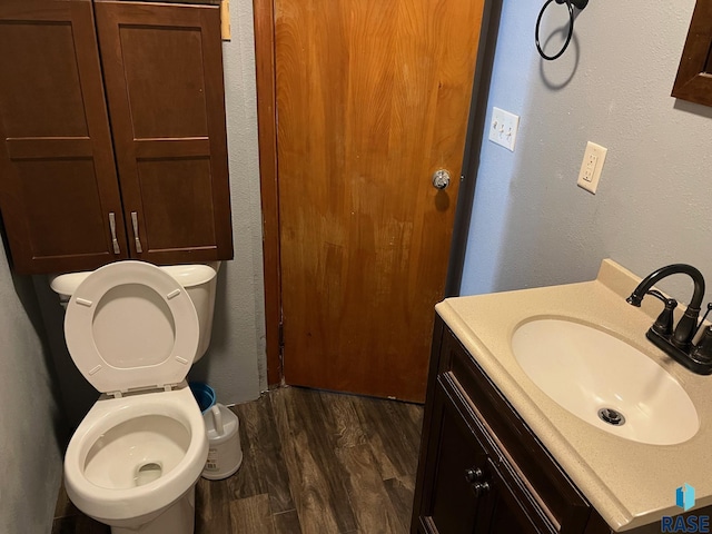 bathroom with toilet, wood finished floors, vanity, and a textured wall