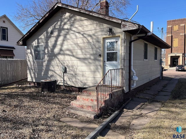 rear view of house featuring entry steps, central AC unit, a chimney, and fence