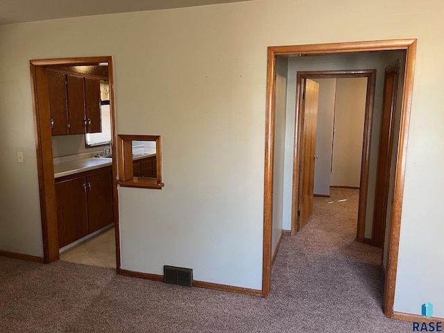 hallway featuring light colored carpet, visible vents, and baseboards