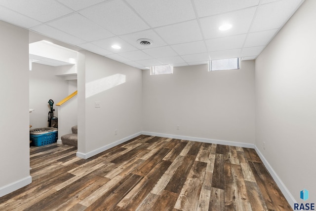 basement featuring visible vents, baseboards, a drop ceiling, stairway, and wood finished floors