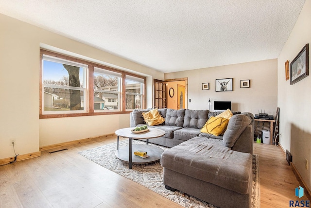 living area with baseboards, a textured ceiling, visible vents, and light wood-type flooring