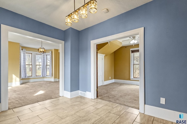 carpeted empty room with wood finish floors, ceiling fan with notable chandelier, and baseboards